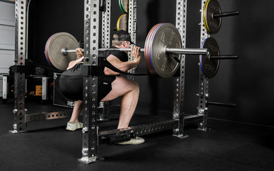 An athlete squatting in a PR-5000 rack in a garage home gym with Rep Fitness Calibrated Steel Plates (KG) loaded on the barbell