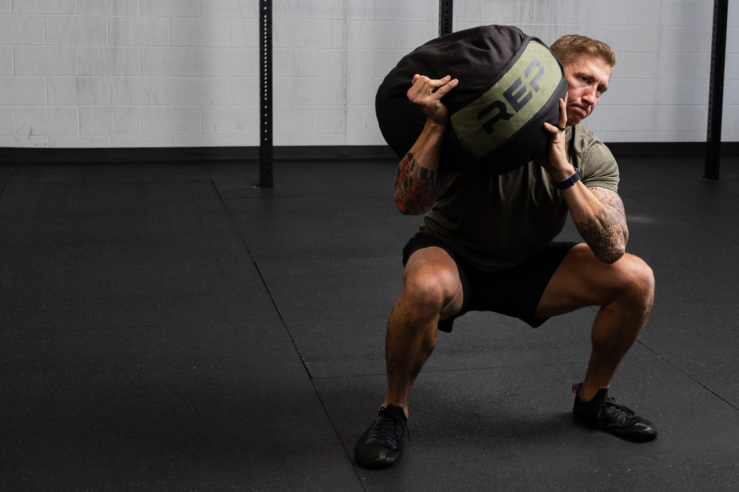 Person performing a squat with a weighted stone sandbag in a gym setting