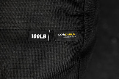 Close-up of a black fabric with '100LB' and 'Cordura' labels on a dark background

