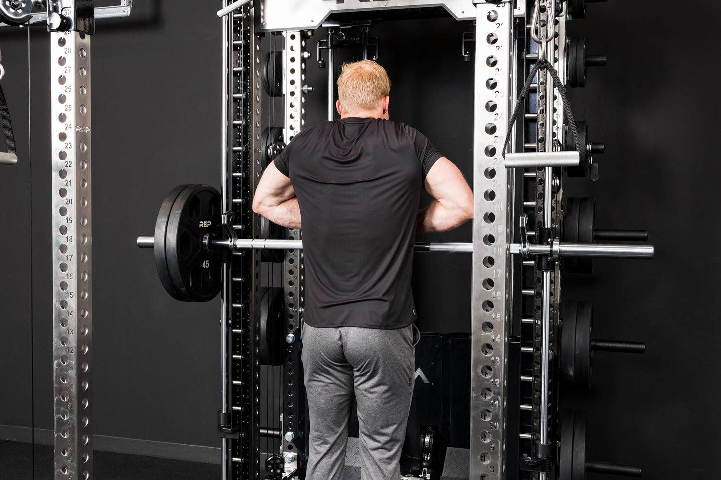 Athlete doing upright rows on the Smith Machine inside a power rack with asymmetrical loading